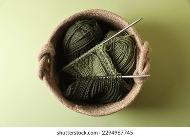 Knitting, needles and soft yarns on light green background, top view