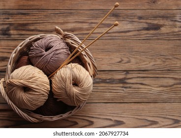 Knitting needles and yarn of beige and brown in a wicker basket on a wooden background. View from above. Handicraft day concept. Place for text.