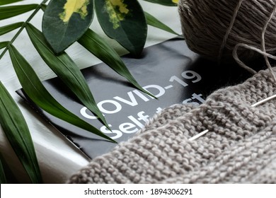 Knitting On Top Of A Covid-19 Self Test Booklet With Green Leaves On One Side