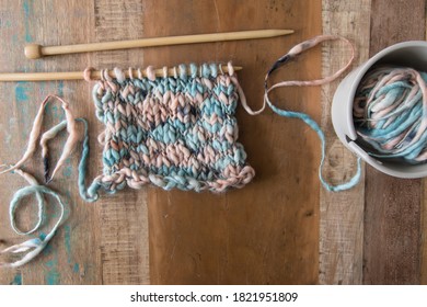 Knitting project using thick and thin chunky pure wool on wooden background with needles