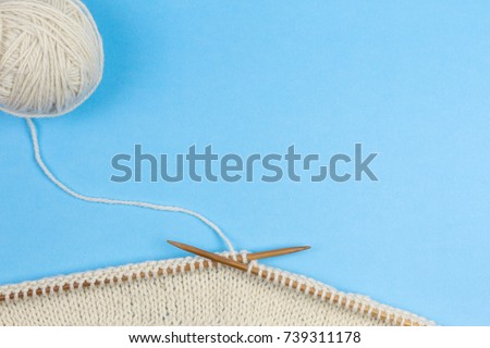 Knitting with wooden knitting needles and wool yarn ball on blue background