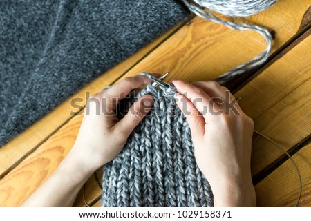 Knitting work: womans hands, swatch and needles close up, wooden background