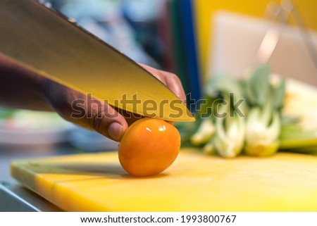 Knive cutting a small tomato on a plastic cutting mat in a kitchen.