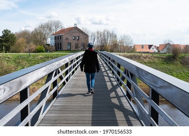 Knokke Heist, Flemish Region - Belgium - 04 03 2021: Active Woman Walking Down A Wooden Pier In A Coastside Nature Reserve