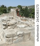 KNOSSOS, CRETE - MAY 8, 2025 - Restored red columns framing north entrance of Knossos Palace, highlighting ancient Minoan architectural design in Cretan landscape