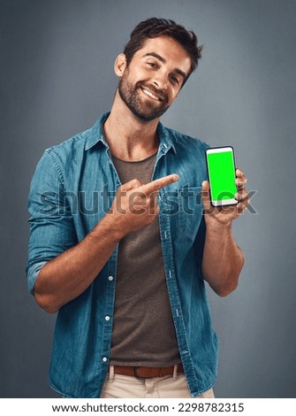 I know a good app when I see one. Studio shot of a handsome young man showing a mobile phone with a green screen against a grey background.