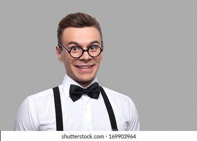 I know a lot of things. Portrait of young nerd man in bow tie and suspenders looking at camera and smiling while standing against grey background