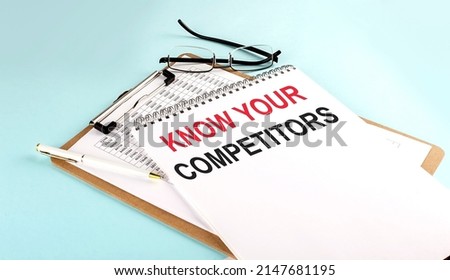 KNOW YOUR COMPETITORS text on notepad on clipboard with chart on a blue background, concept closeup. Business and finance concept