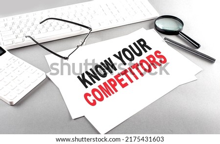 KNOW YOUR COMPETITORS text on a paper on a gray background near a calculator and white keyboard