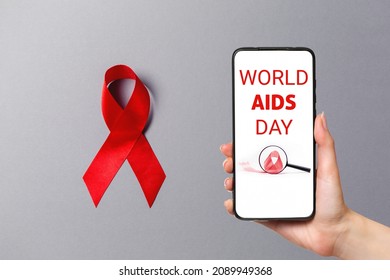 Know your status. A red ribbon on the gray background. Hand holding a smartphone. The concept of world AIDS day.