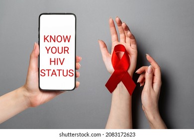 Know your status. Woman's hands, on the palm is a red ribbon. Flat lay. Hand holding a smartphone. Gray background. The concept of world AIDS day.