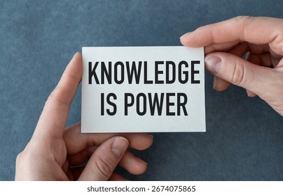 Knowledge is Power close up of a phrase being typed and centered on paper card in hand on gray background