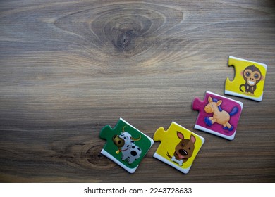 Knowledge puzzles with pictures of smiling monkey, running horse, sitting dog and cow placed on edge of wooden background.
