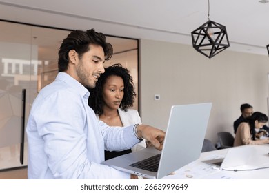 Knowledge sharing in team environment. Smart young man mentor guide consult teach female intern trainee in modern open space office explain business tasks market research results on notebook screen
