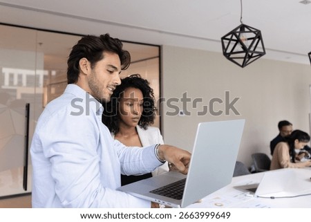 Knowledge sharing in team environment. Smart young man mentor guide consult teach female intern trainee in modern open space office explain business tasks market research results on notebook screen