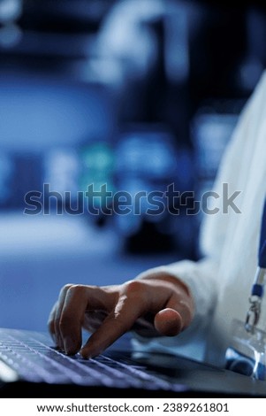 Knowledgeable admin in data center uses laptop to prevent system overload during peak traffic periods. Adept expert in server hub ensuring enough network bandwidth for smooth operations, close up