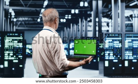 Knowledgeable IT professional navigating network of server racks in industrial hub. Repairman using green screen laptop, ensuring sound operations, doing optimizations and maintenance in data center