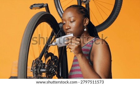 Knowledgeable repairman using specialized glue to recondition broken bicycle chain, orange studio background, cyclist hobbyist applying adhesive on bike parts during inspection process.