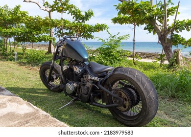 Ko Lanta, Ko Lanta District, Krabi 81150, Thailand  May 14th 2018  A Custom Chopper Motorbike Parked On Grass Next To A Tropical Beach. Rat Bike, Low Rider, Honda Engine