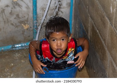 Ko Lanta, Ko Lanta District, Krabi 81150, Thailand  April 18th 2018  A Wet Boy In A Bucket Having A Shower Makes A Funny Face From The Shock Of Cold Water