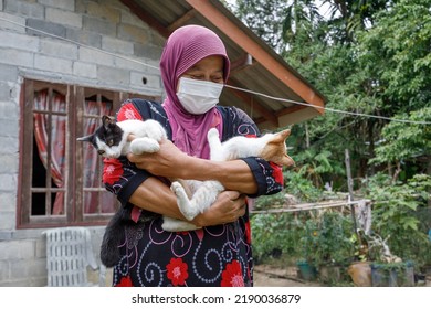 Ko Lanta Noi, Ko Lanta District, Krabi, Thailand  February 11th 2022  A Southern Thai, Muslim Village Woman Holds Her Two Cats In Her Arms, Outdoors In Her Garden With Village House Background