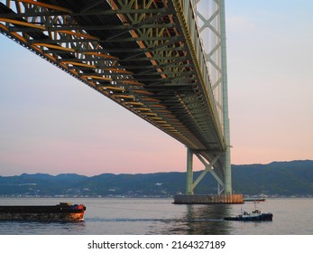 Kobe, Japan, April 29th, 2022: A Tugboat Crossing Under A Suspension Bridge.