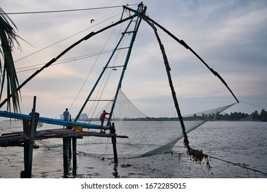 Kochi, India - December 24, 2019: Man Trying To Take Out The Fish From Chinese Fishing Nets Above Water, Near The Empty Shore In The Afternoon, In Kochi, India.