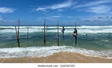 Koggala, Sri Lanka – April 30, 2022: Stilt Fishermen Fishing On A Stick On The Coast Of Koggala, Sri Lanka. 