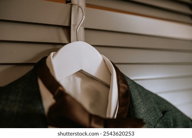 Koknese, Latvia - September 26, 2023 - A close-up of a green suit jacket with a brown bow tie on a white hanger, against neutral shutters, creating a refined and elegant look. - Powered by Shutterstock