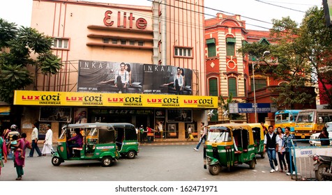 KOLKATA, INDIA - JAN 20: Auto Rickshaw Taxis & Pedestrians Move Past The Old Cinema Theater On January 20, 2013 In Calcutta, India. Indian Three-wheelers Have The Design Of The Piaggio Ape C From 1948