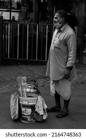 Kolkata, India - January 2, 2022: A tea seller wearing traditional indian dhoti, standing and waiting for customers. A bucket containing tea kettle and paper cups is kept in front. 