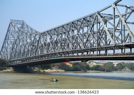KOLKATA, INDIA - MARCH 13: Fisherman boat crosses the Hooghly River nearby the Howrah Bridge on March 13, 2013. Hooghly Bridge is a famous landmark in the city of Calcutta / Kolkata, India.