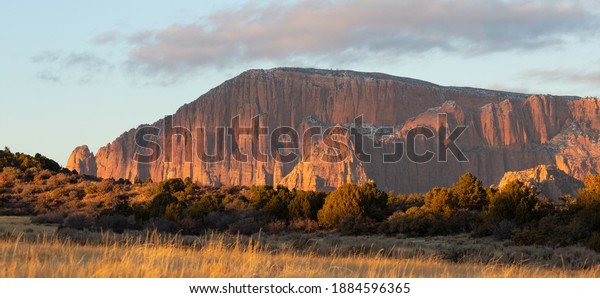 Kolob fingers mountains are lit\
by warm evening light late on a winter day seen from a remote dirt\
road with grassy fields and juniper trees in the\
foreground.