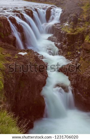 The Kolufoss Waterfall with golden clouds in the sky. The flowing water is captured by a long exposure. Amazing blue color of water from the glacier. Natural and colorful environment.
