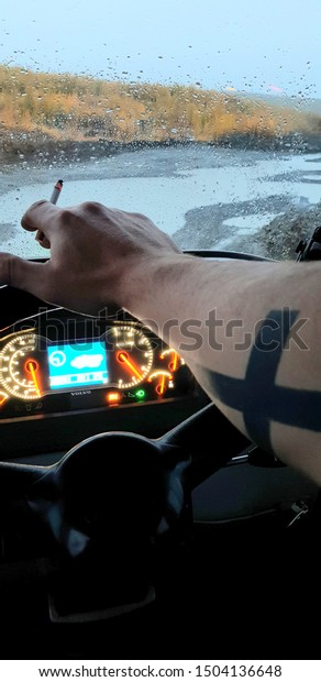 Kolyma, Kolyma / Russia-September 08,\
2019: Hand of a man with a cigarette at the wheel. A man\'s hand\
with a tattoo in a Volvo car. Night outside the\
window.