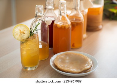 Kombu tea in a glass with ice, lemon slices and rosemary leaves, Homemade fermented raw kombucha tea in bottles and glass jars mix with fruit juice and scoby on table.Healthy natural probiotic drink.