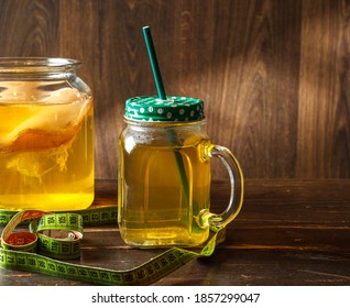 Kombucha Tea In A Glass Cup With A Tube And A Can Of Kombucha, On A Dark Wooden Background With A Measuring Tape