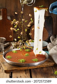 Konafa Traditional Arab, Turkish dessert Kunafa with flying pistachio with sugar syrup on wooden background.