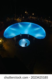 Konakli, Turkey - 06.20.2021: Maintenance Worker Clean Swimming Pool At Hotel Resort With Stick, Human Silhouette At Illuminated Water Background