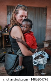 Kongo Village / Ghana - 02.24.2015: A Volunteer Working In Ghana Holding And Kissing A Cute Ghanaian Baby Boy Wearing A Red Shirt.