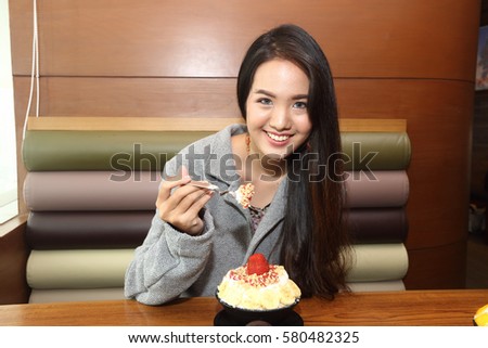Korea Sweet Ice dessert famous with fruit colorful topping with milky sauce on wood table, woman enjoy eating modern popular new menu bingsu