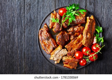 Korean Braised Pork Ribs With Red Pepper Flakes, Cherry Tomato, And Parsley On A Black Plate On A Dark Wooden Background, View From Above, Copy Space