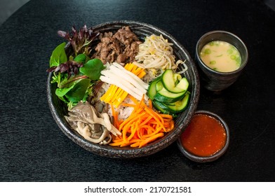 Korean Bulgogi Bibimbap, marinated beef bento box hot stone bowl with salads, kimchi, Bibimbap sauce, miso soup on black table background