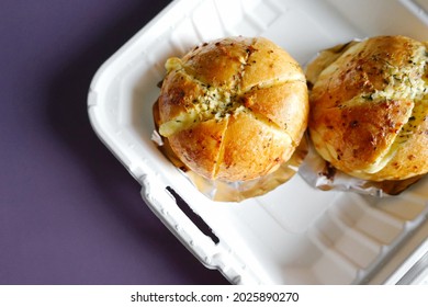 Korean Cream Cheese Garlic Breads Over Aluminum Foil Baking Sheets Contained In Biodegradable Leakproof Take Out Food Boxes On Purple Background. (top View, Selective Focus, Space For Text)