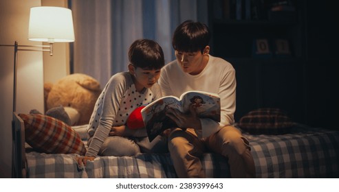 Korean Father Reading a Fairytale to His Lovely Cute Son in Bed Before Going to Sleep. Patient Father Helping his Son to Learn how to Read his Favorite Book. Parent and Child Bonding Moment - Powered by Shutterstock