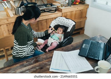 korean female freelancer taking time from work is giving solid food to baby in her study. asian woman working from home needs to care her child during daytime. - Powered by Shutterstock