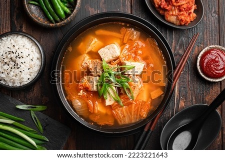 Korean food, kimchi soup with tofu in a ceramic bowl on a wooden background, top view