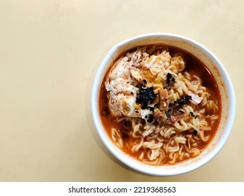 Korean Food Tteok Ramyeon (Rice Cake Ramen) In White Paper Bowl. Yellow Table Surface Background. Negative Space 