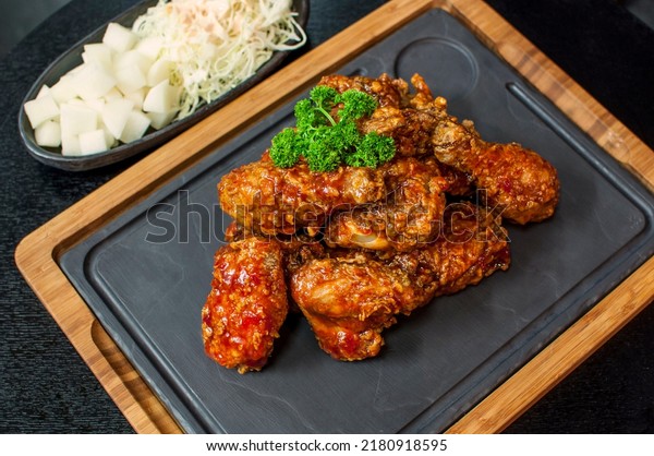 Korean Fried Chicken with Sweet Spicy Sauce,\
traditional Korean fried chicken on grill plate with pickle dishes\
on black table\
background