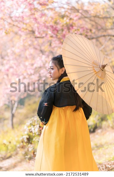 Korean girl wearing a hanbok wearing yellow\
umbrella. Beautiful Female wearing traditional Korean hanbok with\
cherry blossom in spring, seoul,\
Korea.